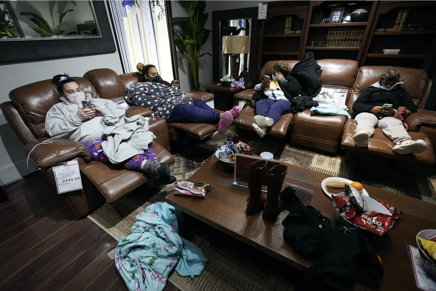 People bundled in blankets sit on chairs in a furniture showroom. People with no power at their homes rest inside a Gallery Furniture store in Houston after the owner opened the business as a shelter on Feb. 16, 2021.  AP Photo/David J. Phillip